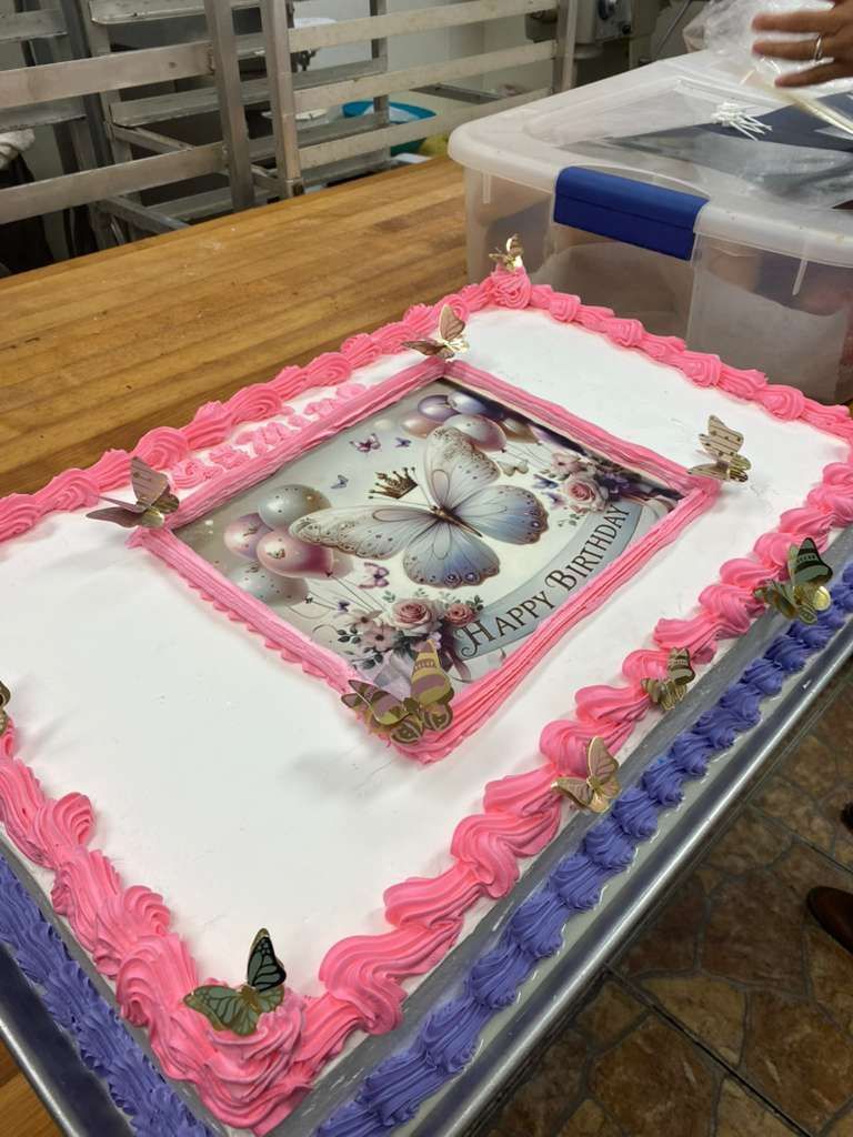 A rectangular cake decorated with pink and purple frosting borders, butterfly accents, and a central birthday image.