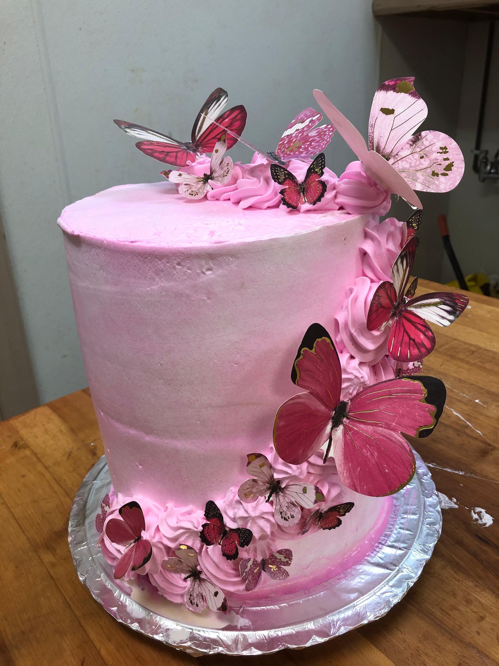 A tall, pink-frosted cake decorated with cascading pink and white butterfly cutouts and piped frosting on the side.