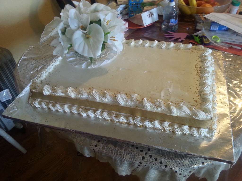 A rectangular sheet cake with white frosting and a border of piped cream, decorated with white calla lilies.