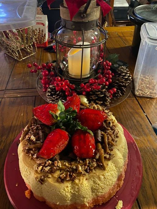 A cheesecake topped with fresh strawberries and pecans on a red plate, next to a festive lantern centerpiece.