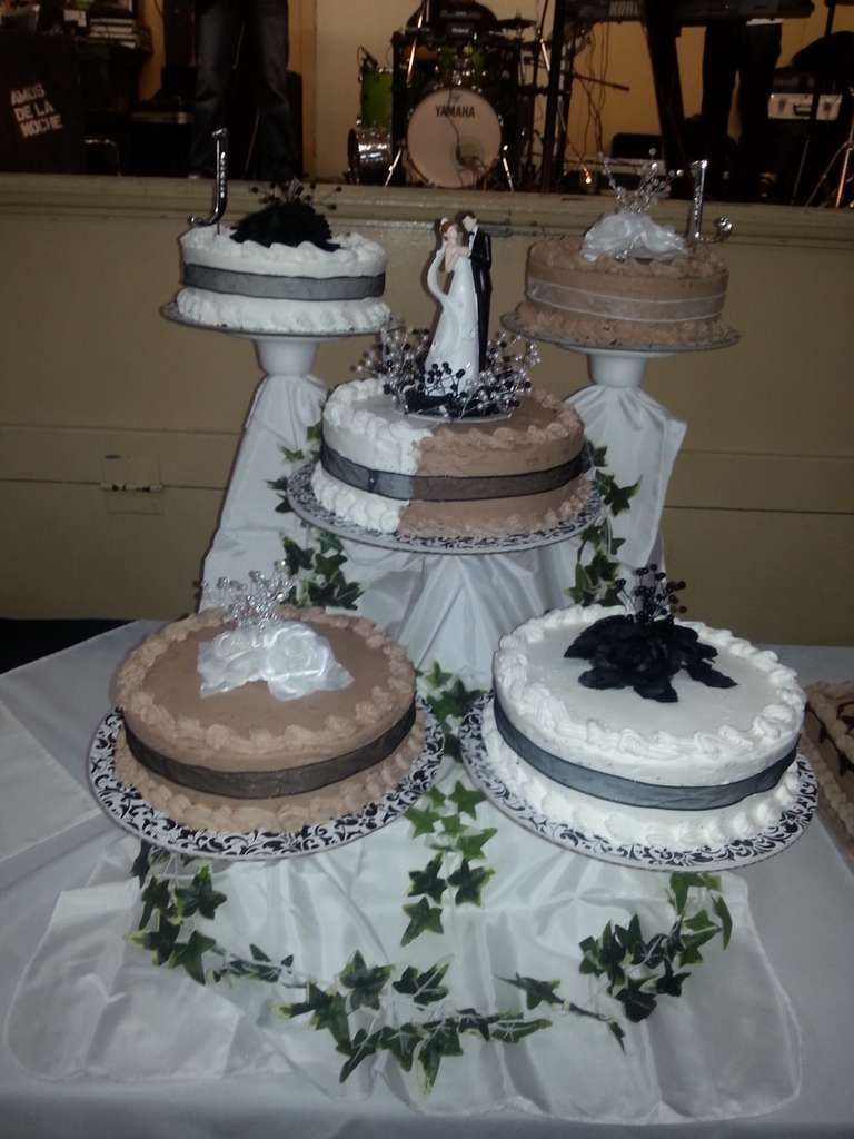 Five round wedding cakes on tiered pedestals, decorated with black and white ribbons, floral accents, and a cake topper.