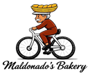 A person with a mustache wearing a brown uniform rides a white bicycle while balancing a basket of bread on their head.