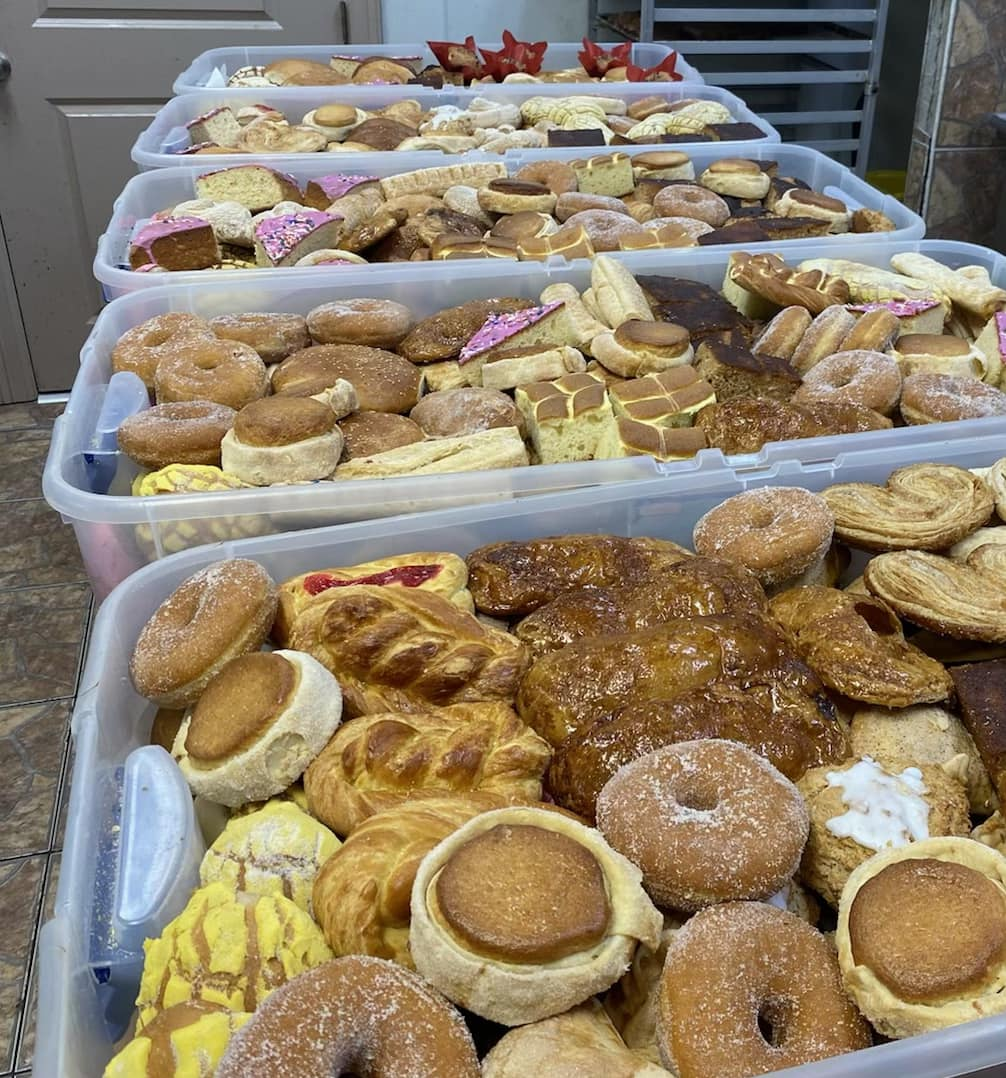 Several plastic bins filled with an assortment of donuts, pastries, and baked goods stacked on a table.