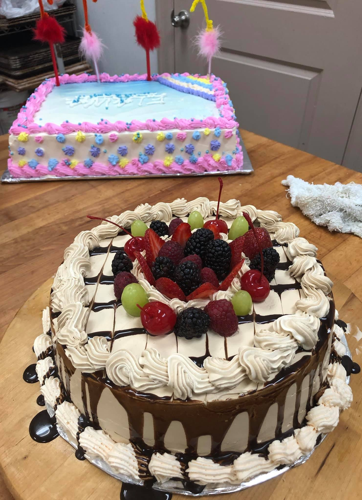 Two birthday cakes on a wooden table: a round chocolate cake topped with berries and a rectangular cake with decorations.