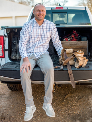 Man smiling, leaning on a counter, wearing a white and blue checkered shirt. Indoor setting.