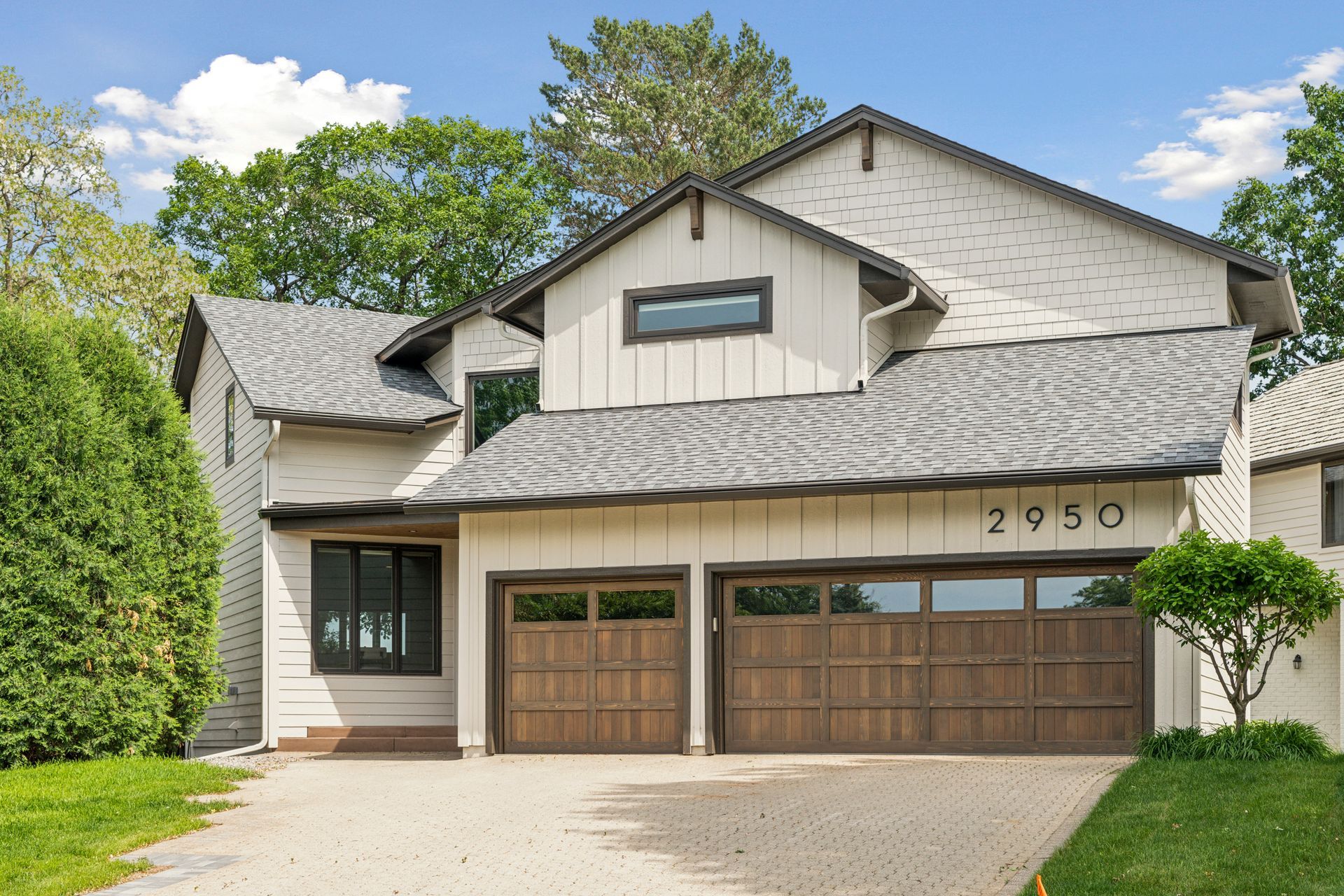 Two-story house with brown garage doors, white siding, and a driveway, under a blue sky.