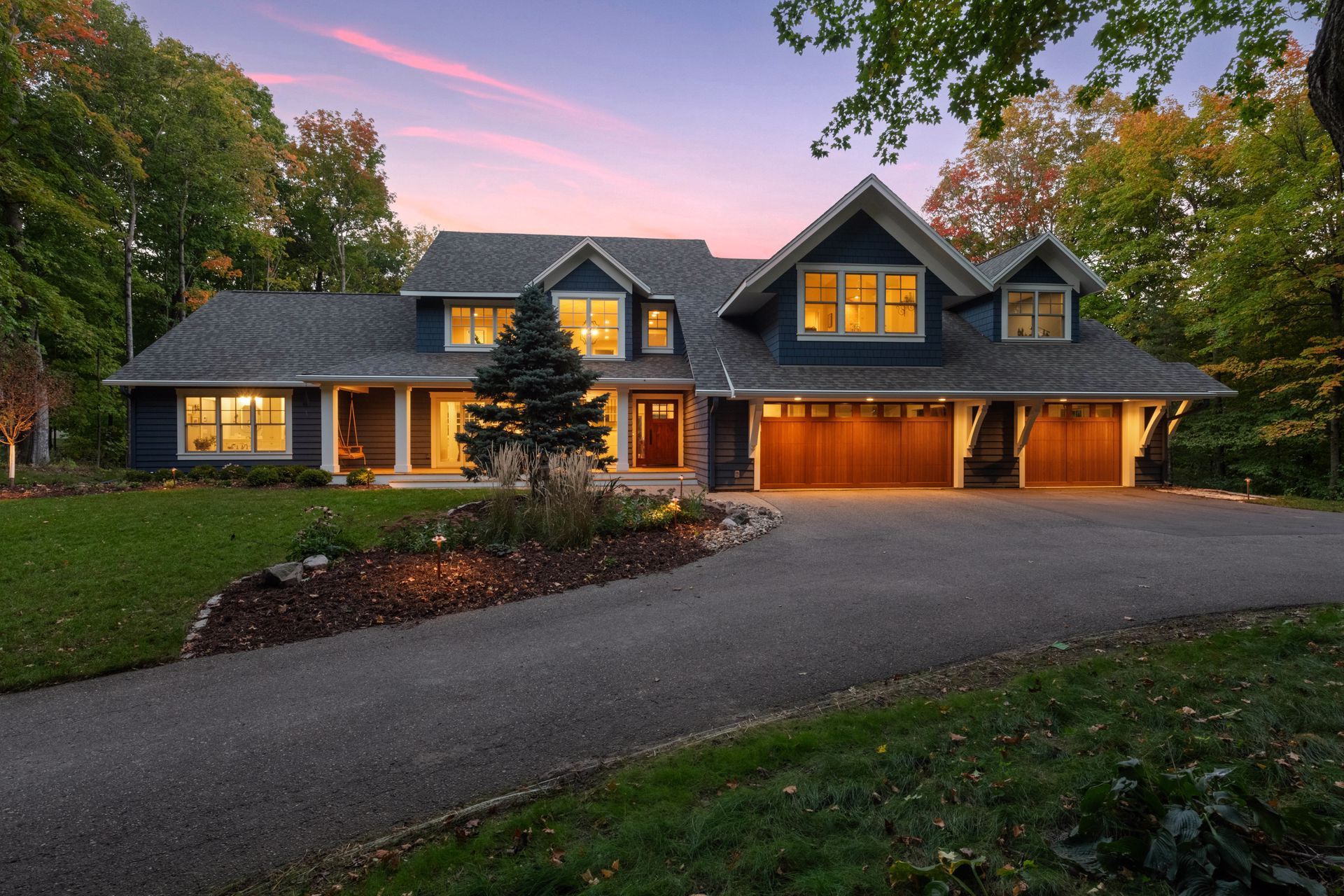 Blue house with wooden garage doors, driveway, and colorful dusk sky.