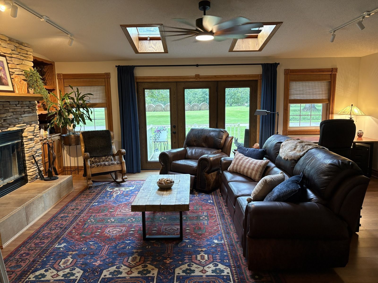 Cozy living room with leather sofas, fireplace, patterned rug, and French doors to a green yard