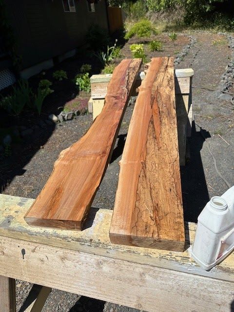 Two reddish-brown wood slabs resting on a weathered workbench outdoors, likely for a woodworking project.