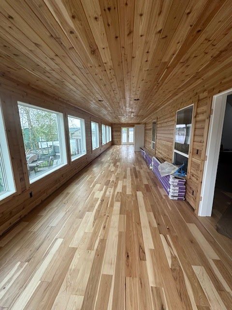 A sunroom with light wood floors and walls. Large windows look outside, and the ceiling is cedar.