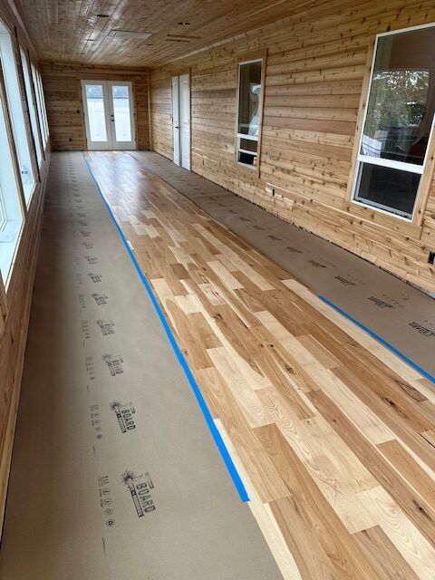 Newly installed hardwood floor in a sunroom, protected by paper. Wood walls, ceiling, and windows.