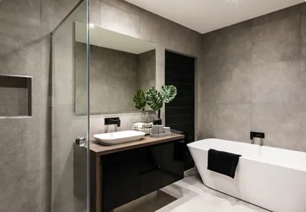 Modern bathroom with a black vanity, white tub, and gray tiled walls.