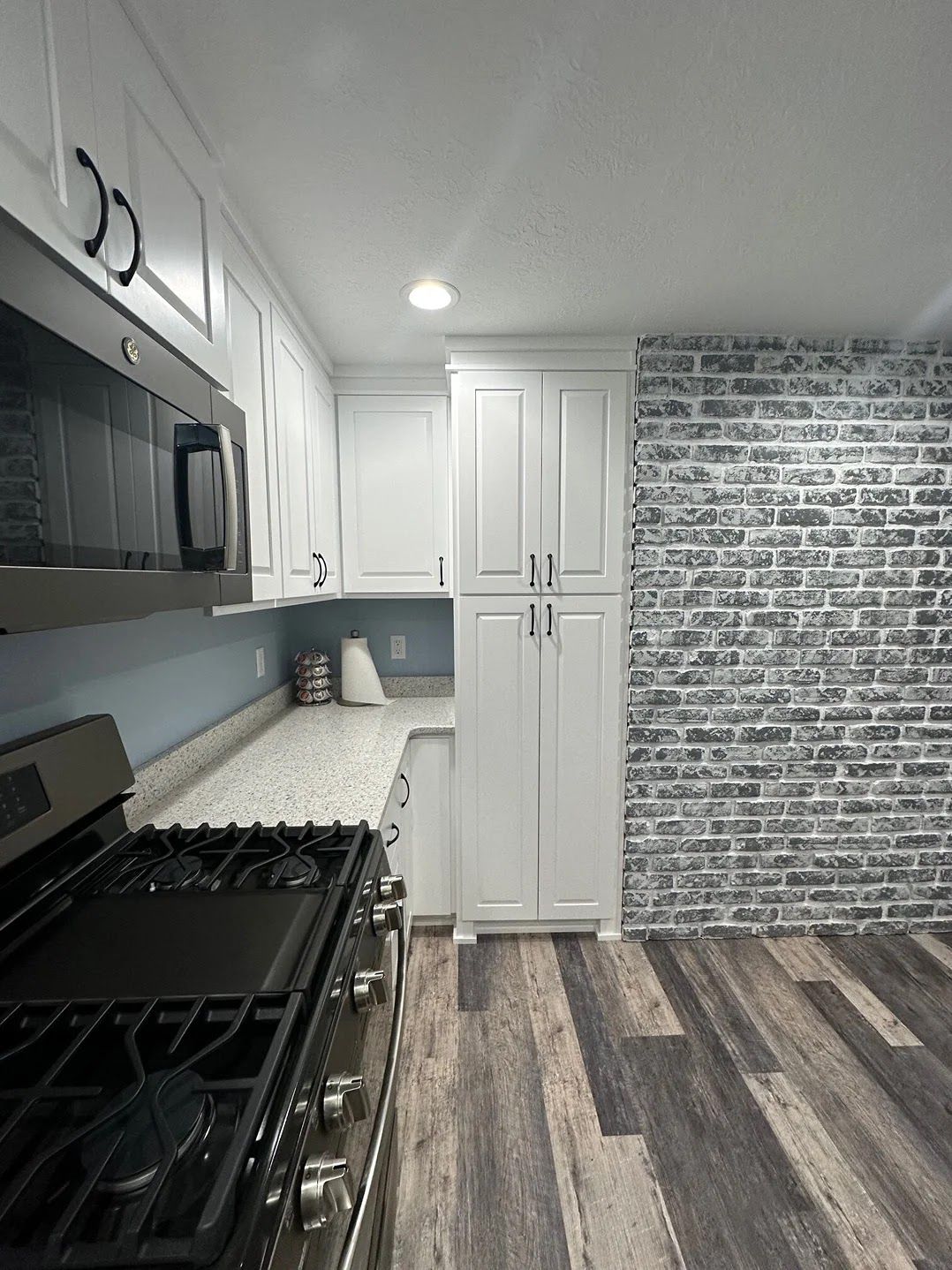 White kitchen with a brick accent wall, gas stove, and wood-look flooring.