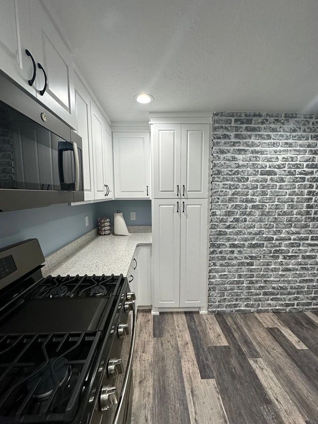 White kitchen with gas stove, granite countertops, and brick accent wall.