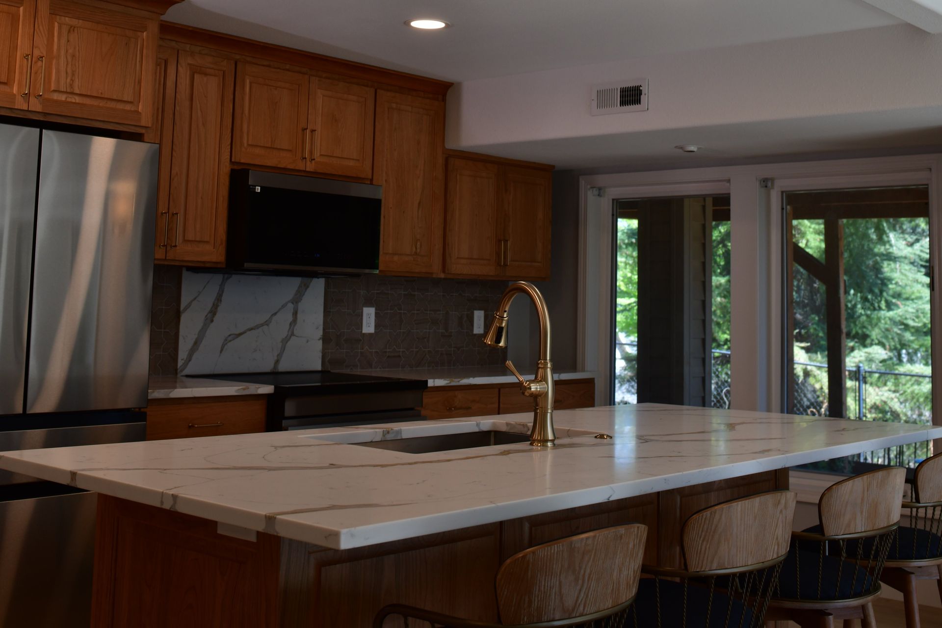 Kitchen with wood cabinets, white countertops, stainless steel appliances, and island with bar stools.