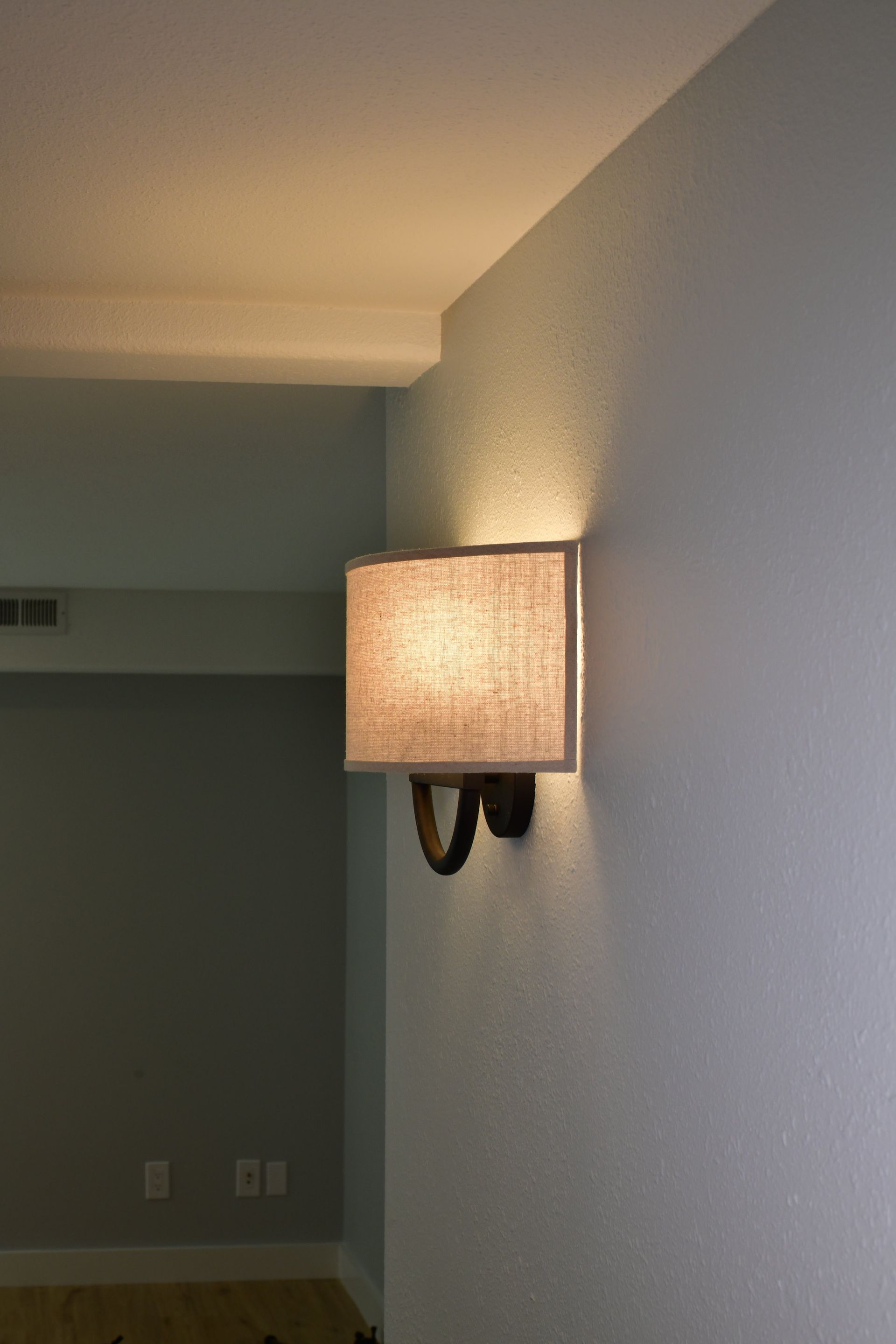 Wall sconce with tan shade lit, casting a warm glow on light blue wall.