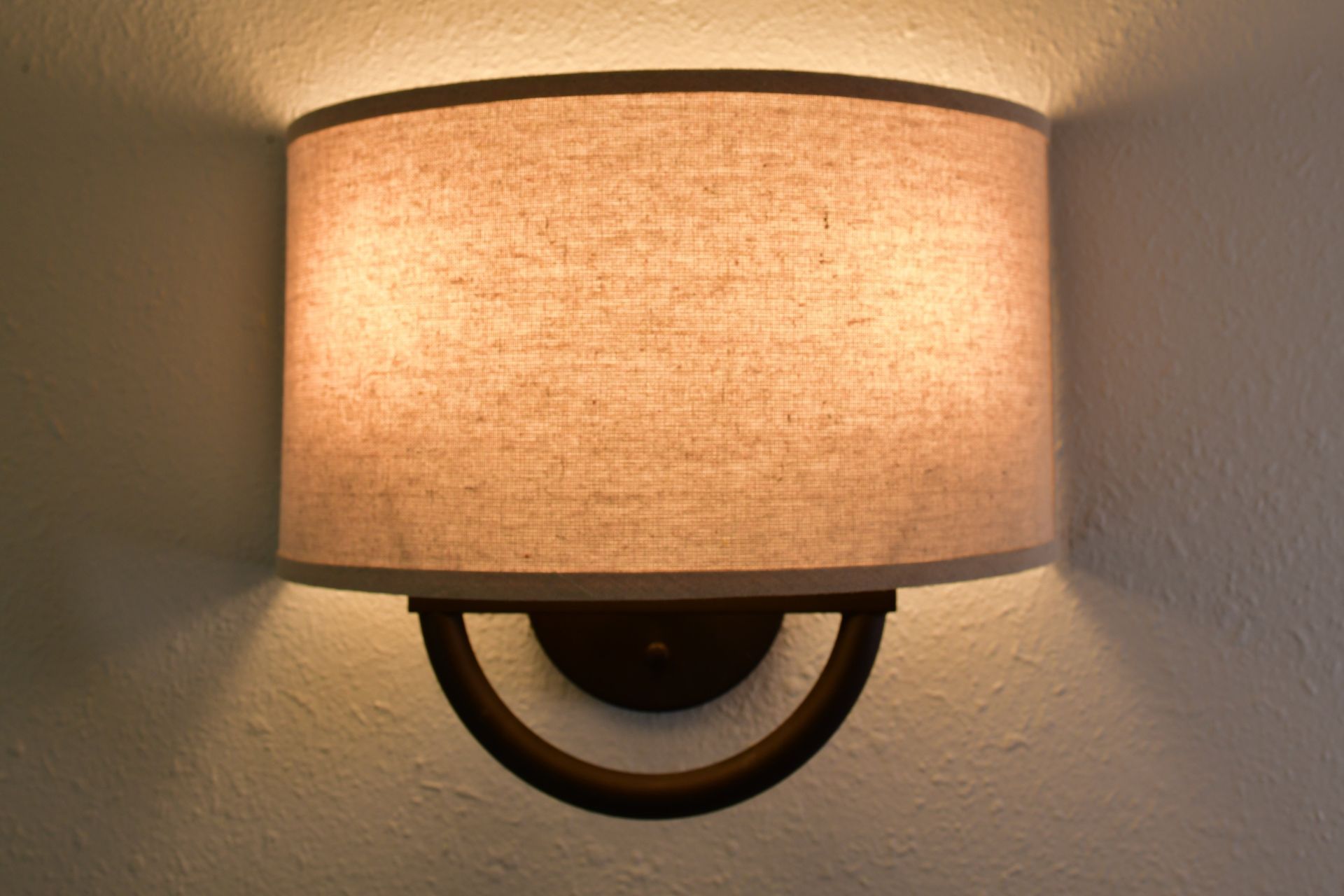 Wall-mounted lamp with tan shade, dark brown bracket, and light cast on a white wall.