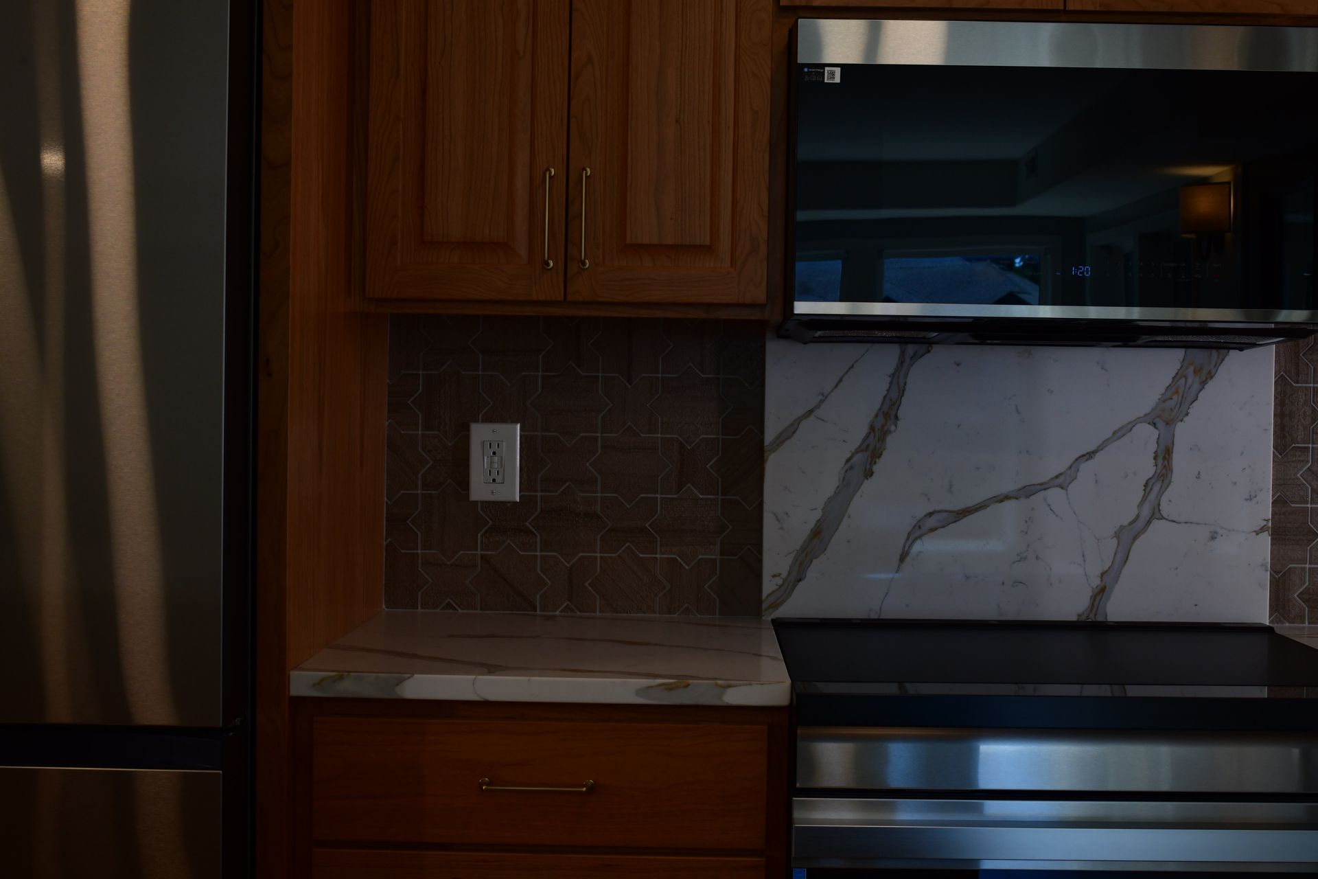 Kitchen with wood cabinets, marble countertop, dark backsplash, and stainless steel appliances.