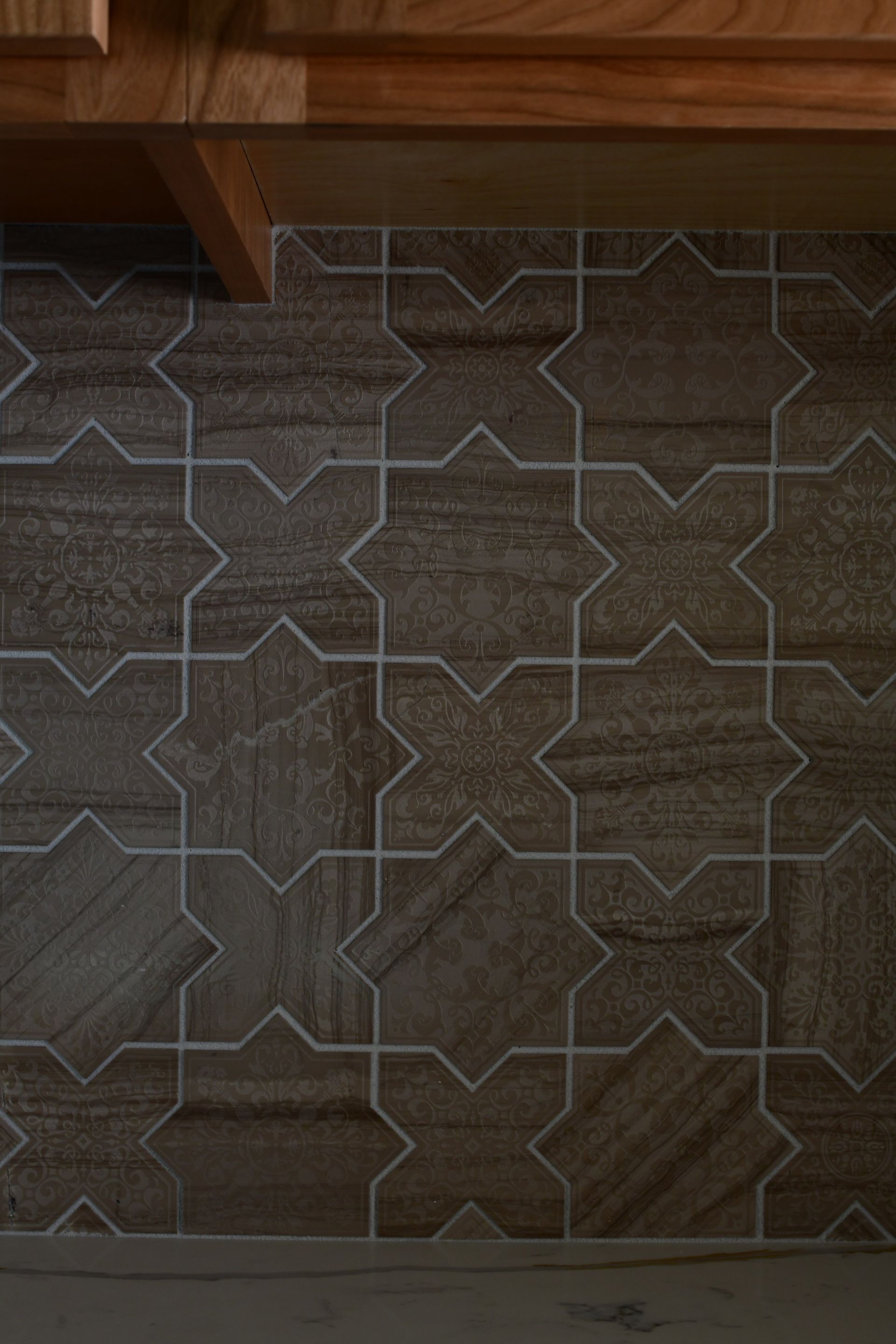 Brown and tan star-patterned tiles on a wall below wooden cabinets, with white grout lines.