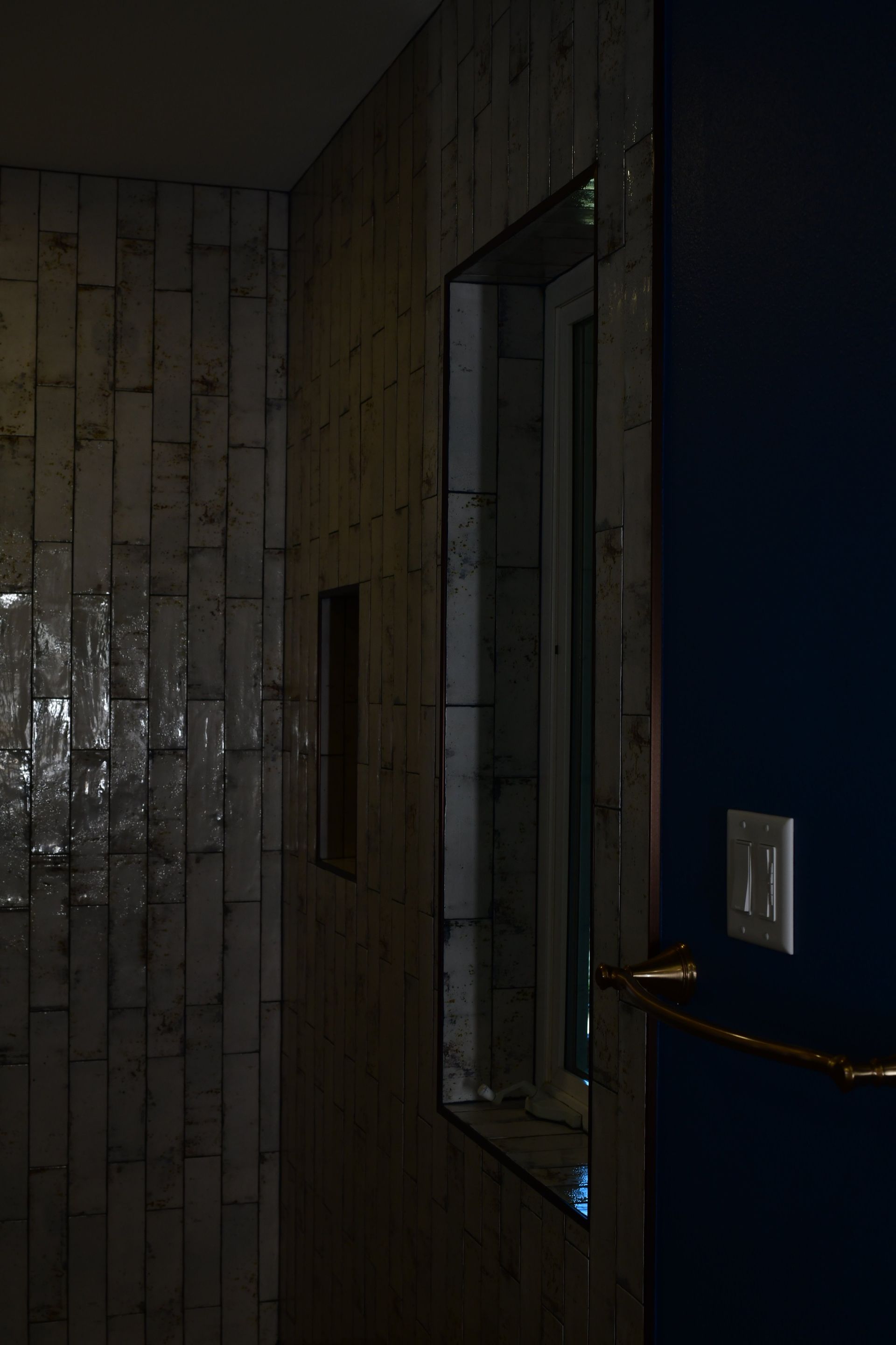 Wood-paneled shower with a small window and blue wall; gold towel bar and light switch.