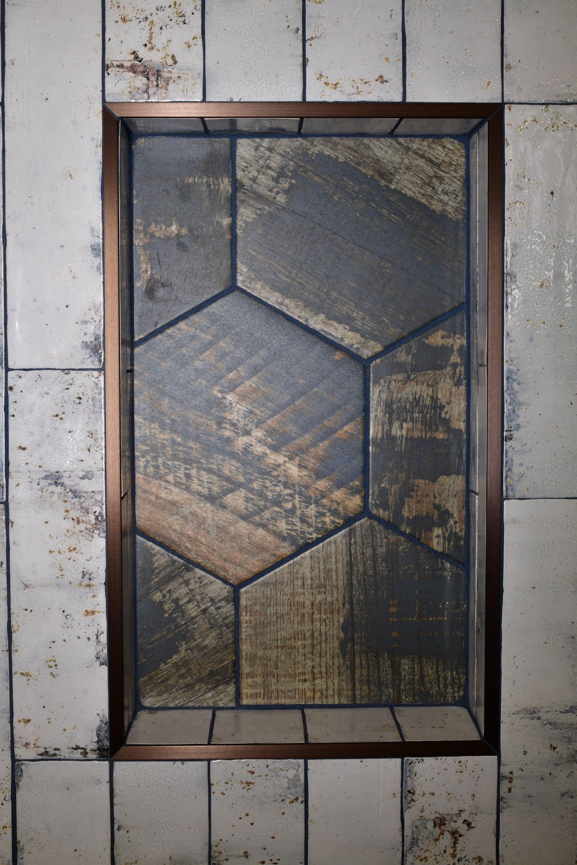 Bronze-framed inset of hexagonal rustic tiles, set into a white, textured tiled wall.