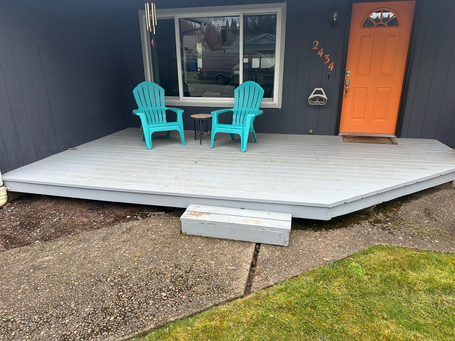 Gray house front with teal chairs on a light gray deck, orange door.