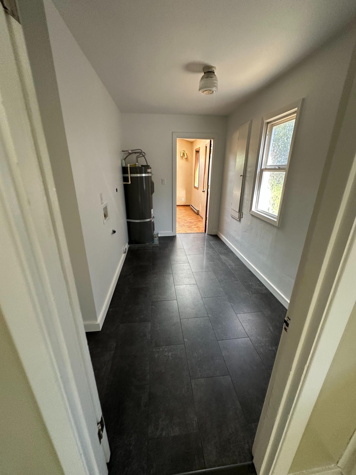 Narrow laundry room with dark flooring, water heater, and a doorway leading to a hallway.