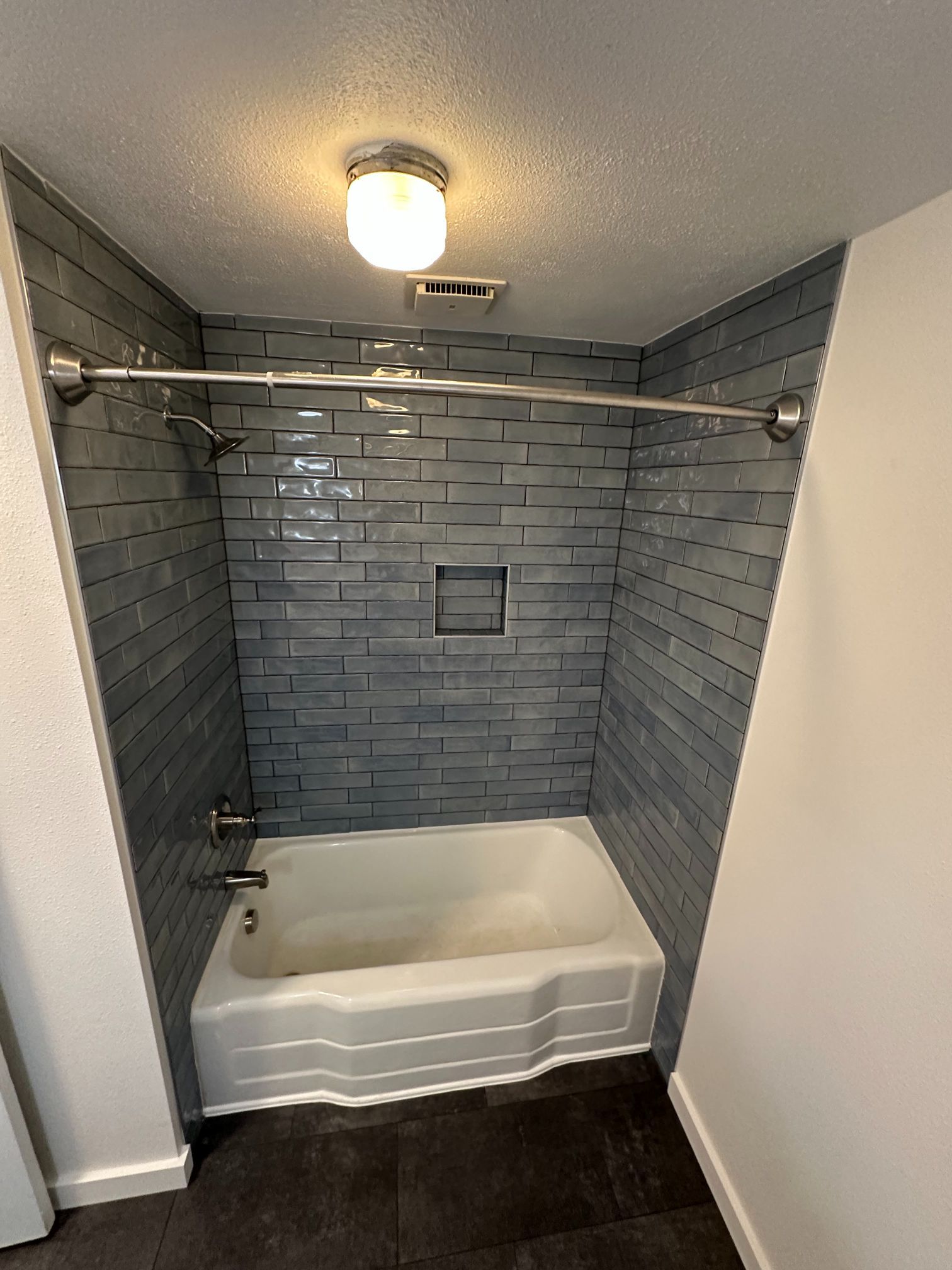 Compact bathroom tub alcove with blue-gray tile, white tub, shower rod, and ceiling light