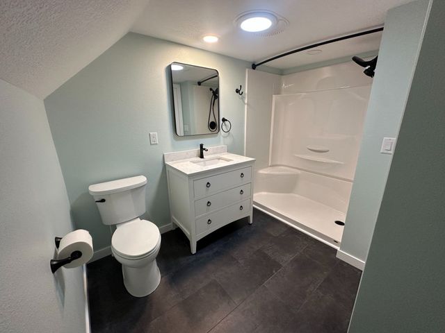 Bathroom with white vanity, toilet, and shower stall; light blue walls and dark gray tile floor.