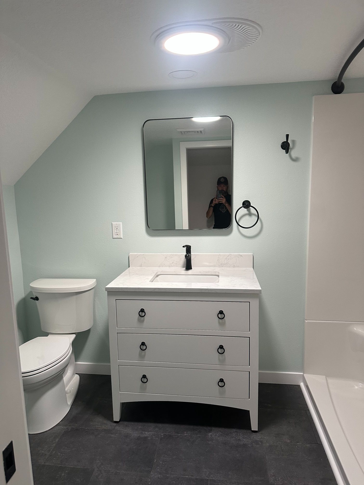 Bathroom with mint green walls, white vanity, black fixtures, dark floor. Toilet on left.