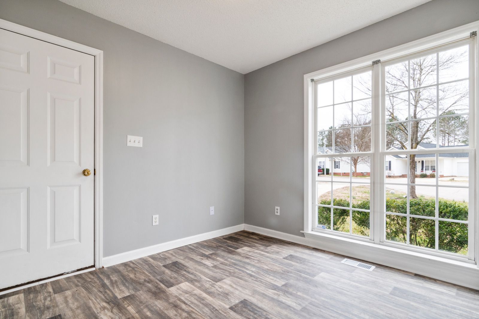 Empty room with gray walls, a white door, a large window, and wood-look flooring.