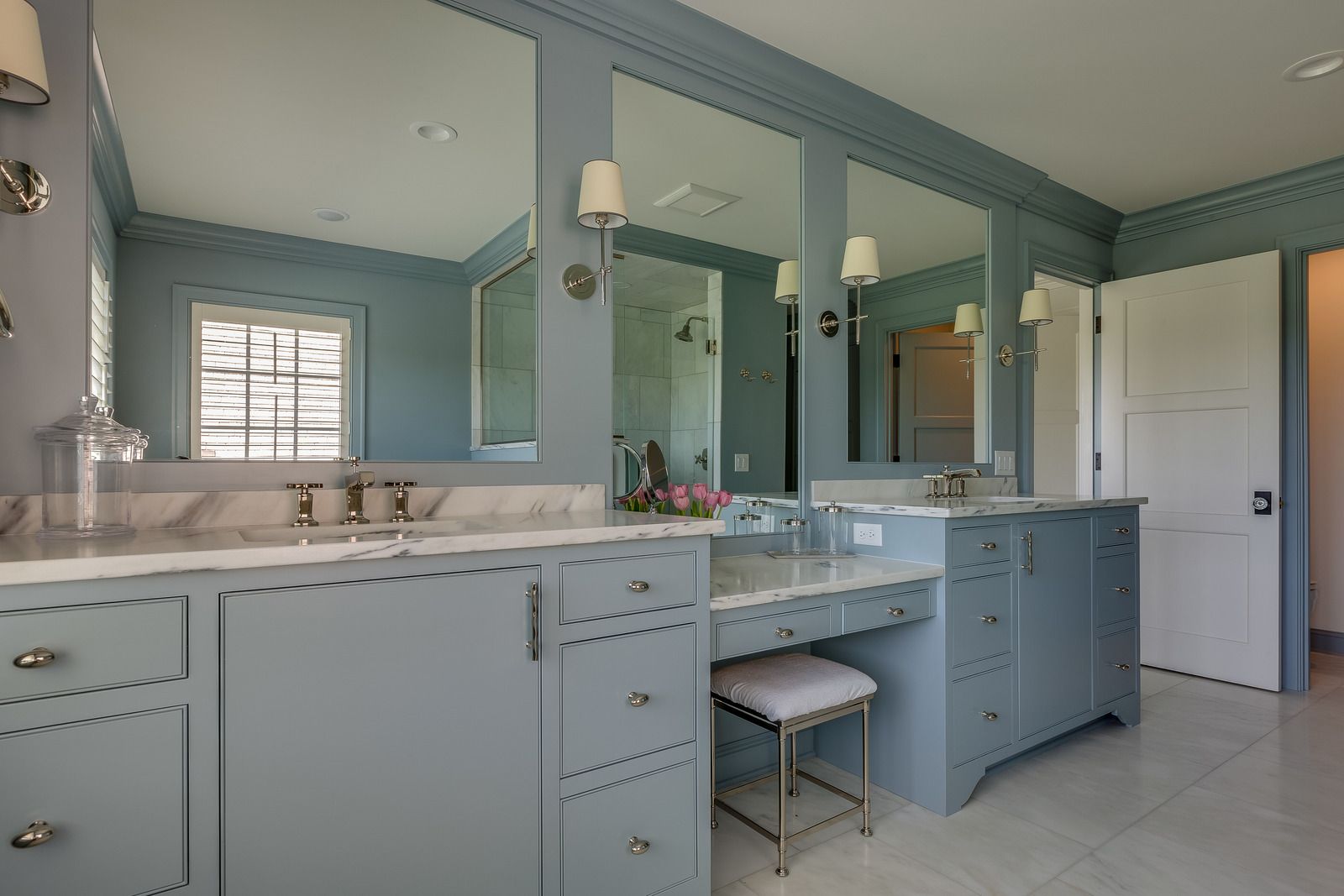 Blue bathroom with three mirrors, double sinks, a vanity, and a white door.