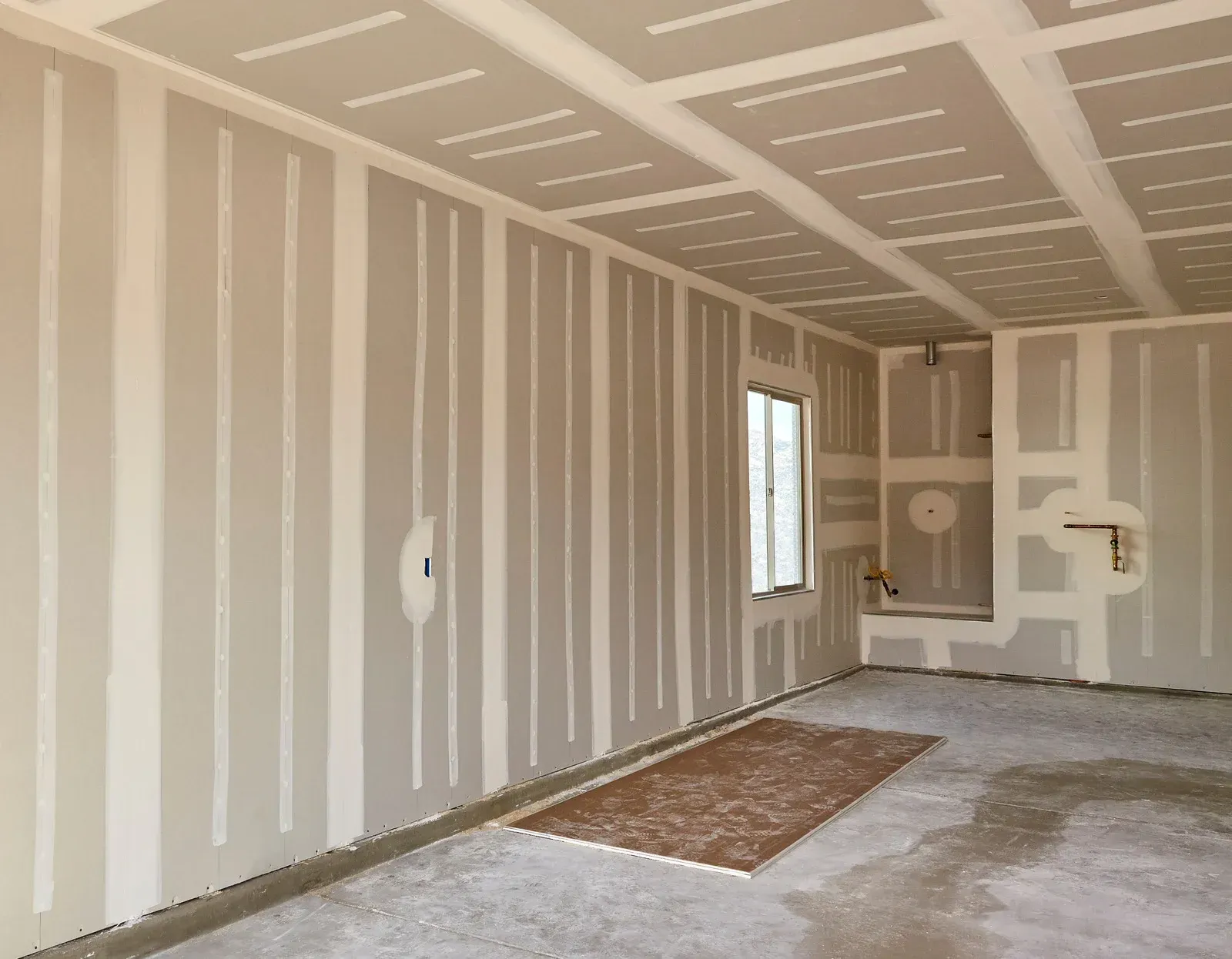 Interior room with drywall installed on walls and ceiling; a window and exposed framing.