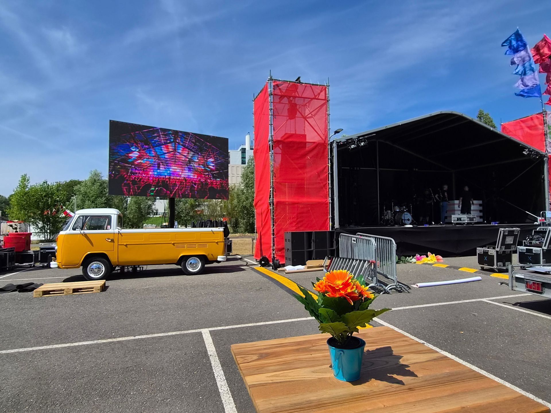 Opstelling van een openluchtconcertpodium met een gele volkswagen T2 met groot led scherm.