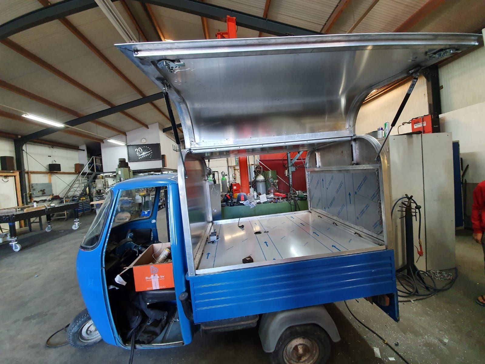 Blauwe piaggio met open laadbak in een werkplaatsgarage