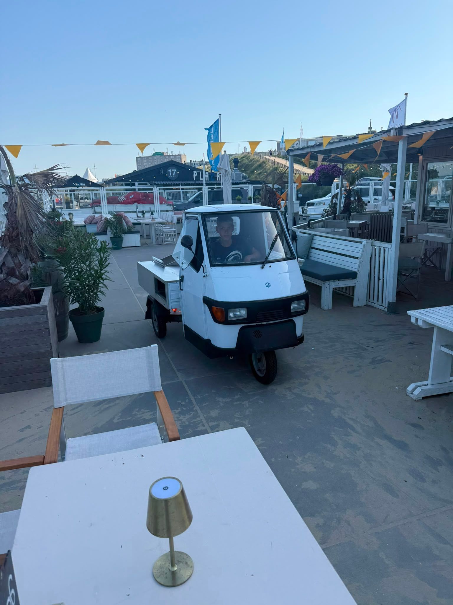 Een kleine witte piaggio in een terrasje aan zee, bij schemering.