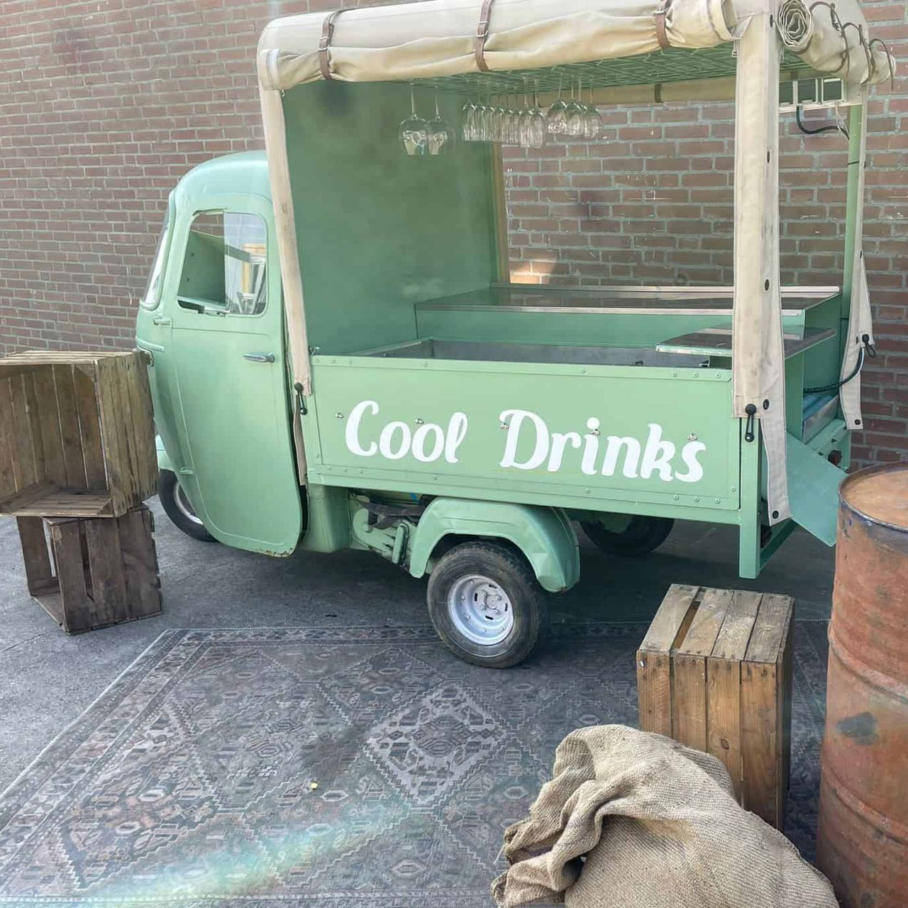 Een mintgroene mobiele drankkar met de tekst "Cool Drinks" op de zijkant, geparkeerd tegen een bakstenen muur.