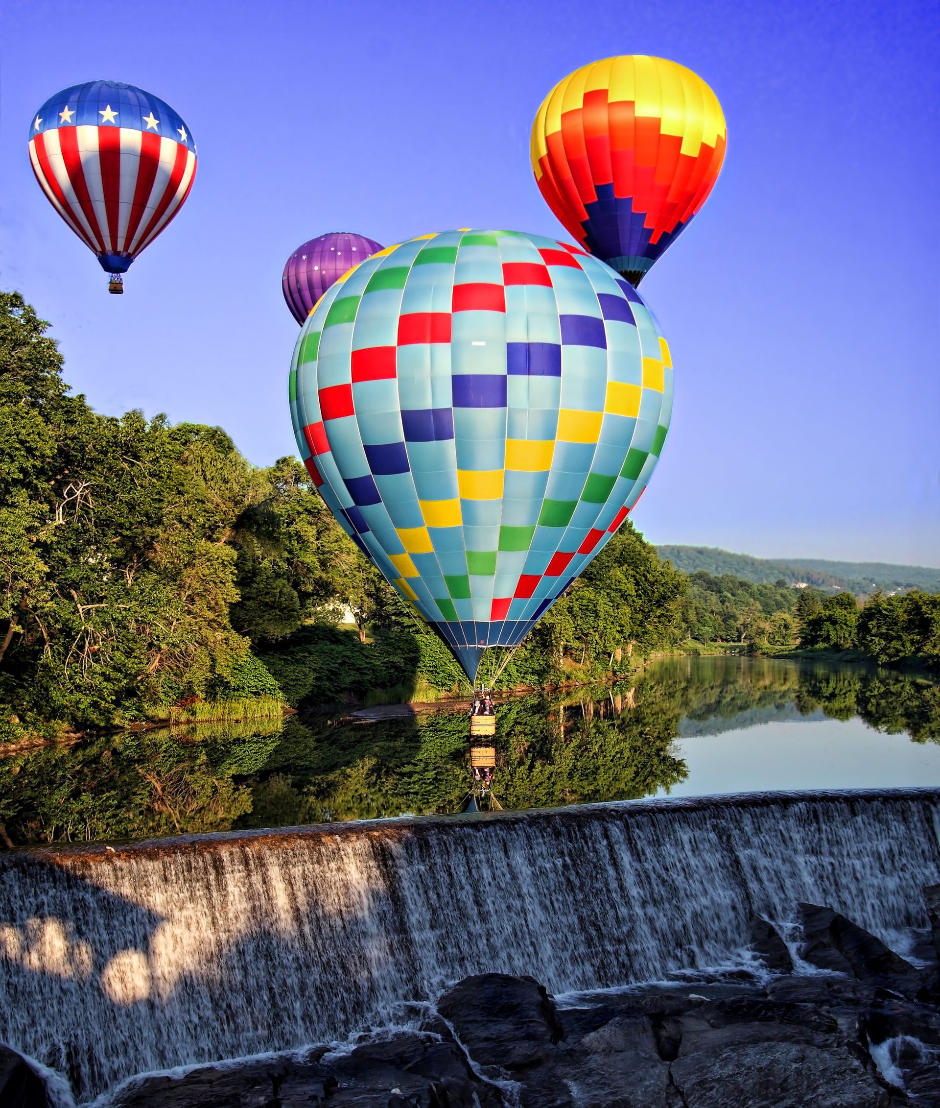 Colorful hot air balloons floating over a waterfall and river at sunrise