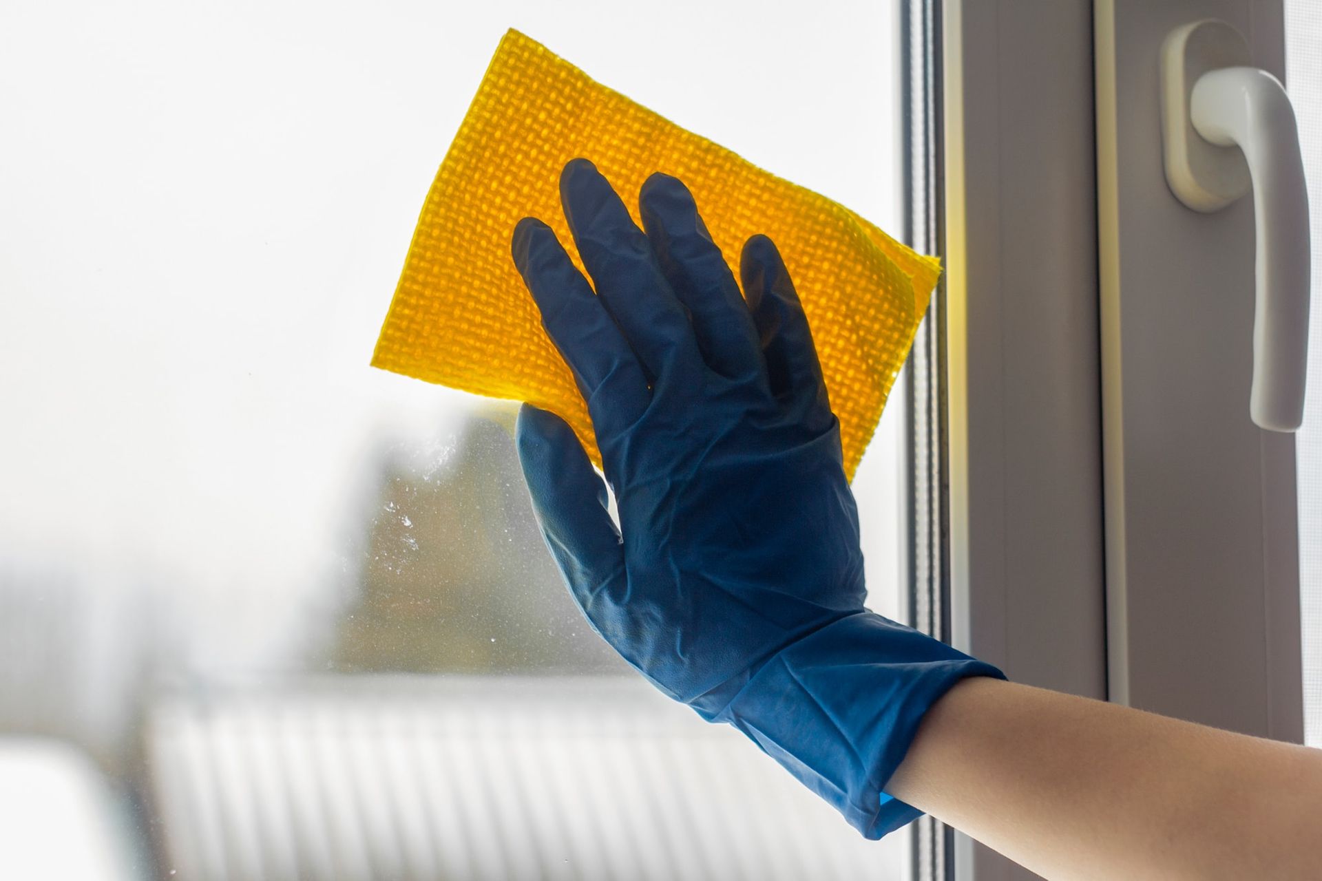 A person wearing blue gloves is cleaning a window with a yellow cloth.