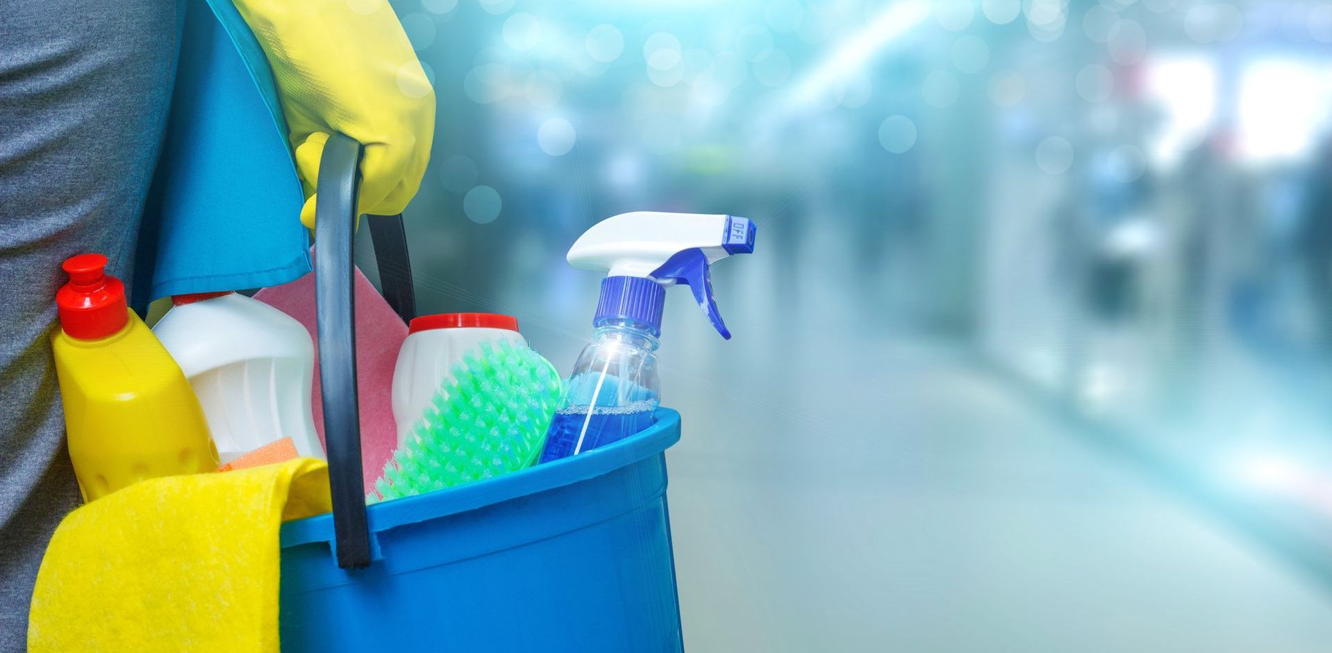 A person is holding a blue bucket filled with cleaning supplies.