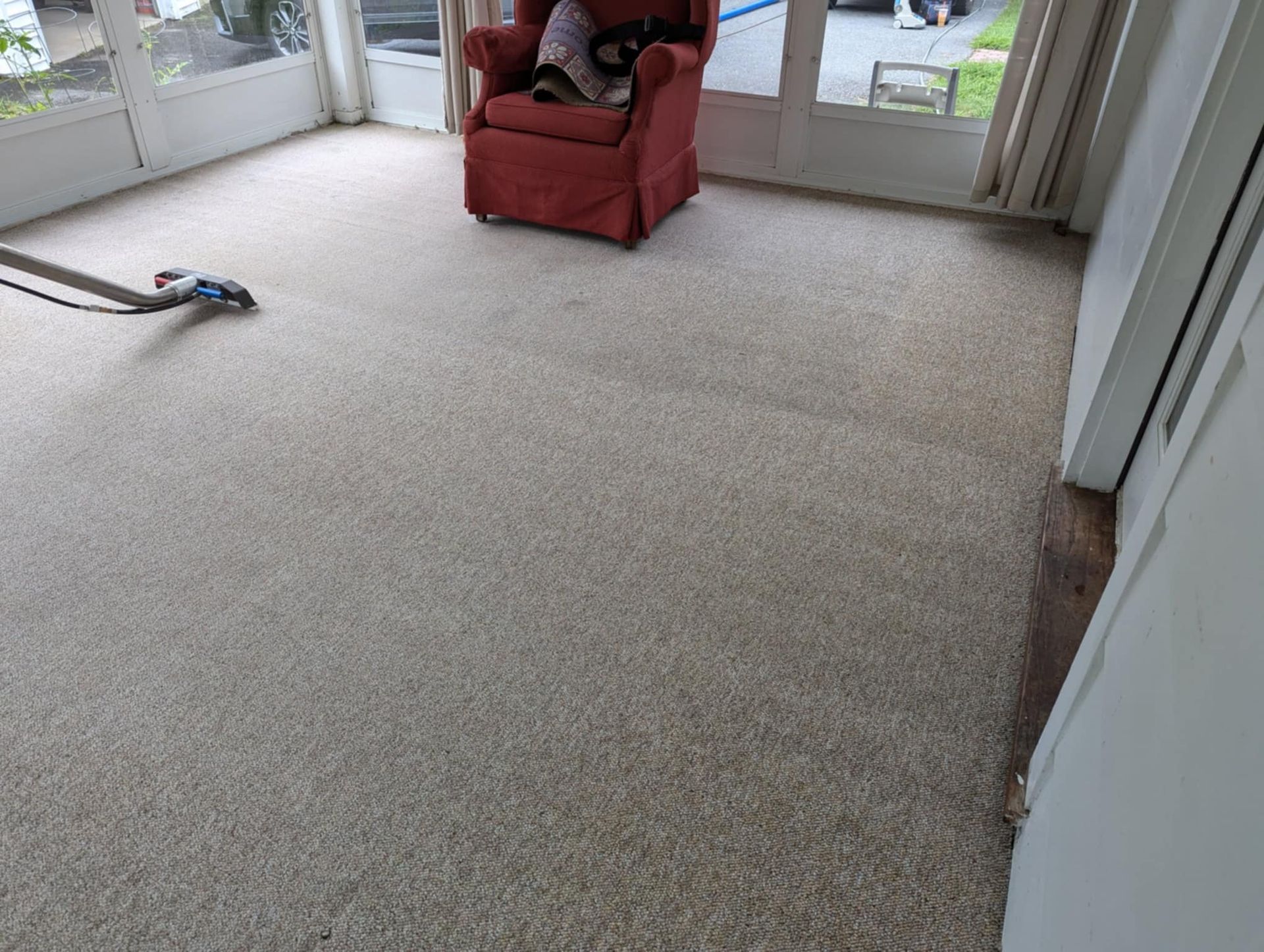 A living room with a red chair and a vacuum on the floor.