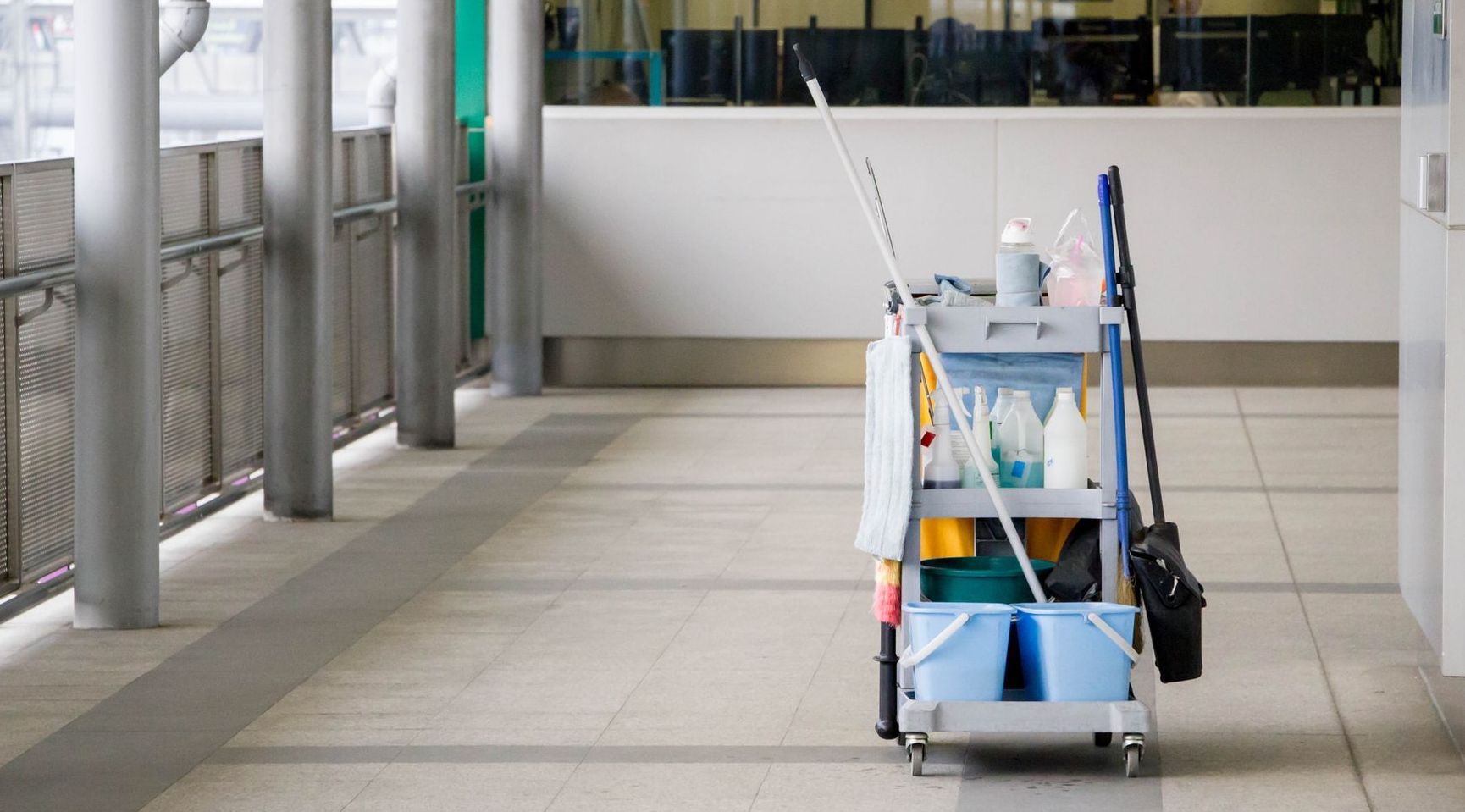 A cleaning cart with cleaning supplies and a mop is sitting in a hallway.
