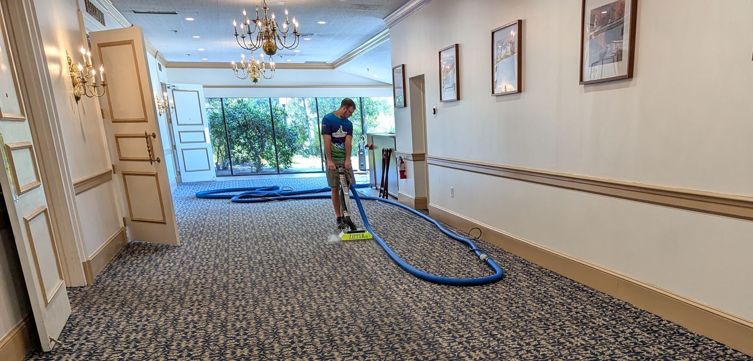 A man is using a steam cleaner to clean a carpet in a hallway.