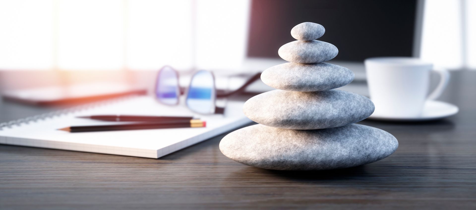 A stack of rocks is sitting on a desk next to a cup of coffee and a notebook.