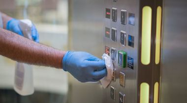 hotel cleaning services image of a janitor cleaning the elevator buttons in the lobby of a hotel