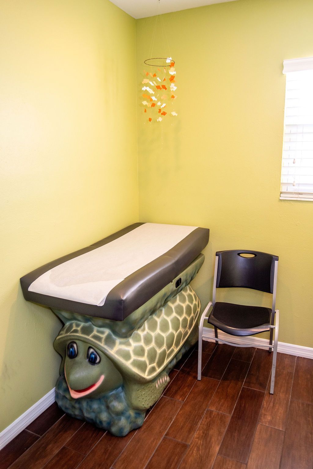 A turtle shaped examination table is in a room next to a chair.