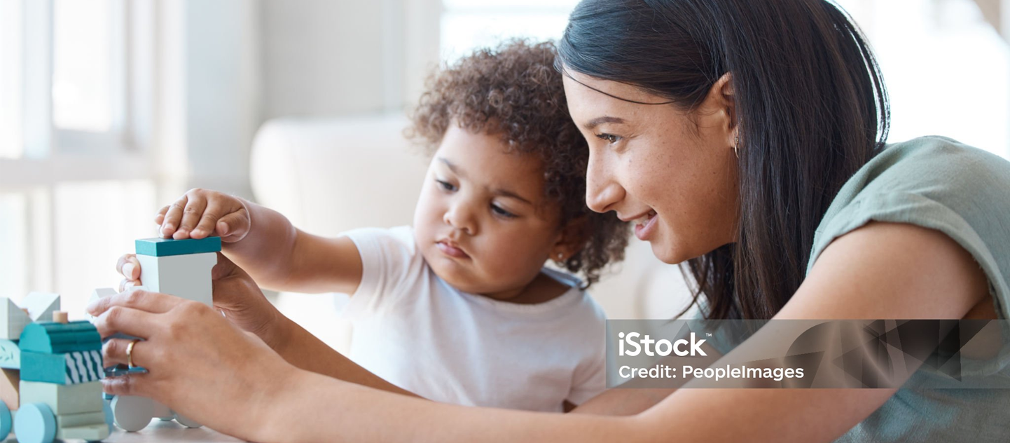 A woman and a child are playing with blocks at a table.