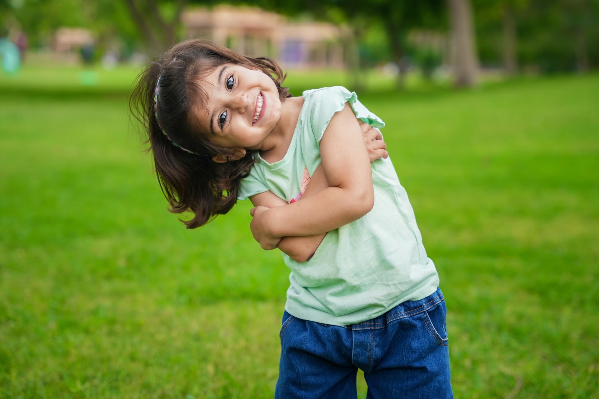 Little girl leaning sideways in a park with green grass in the background.