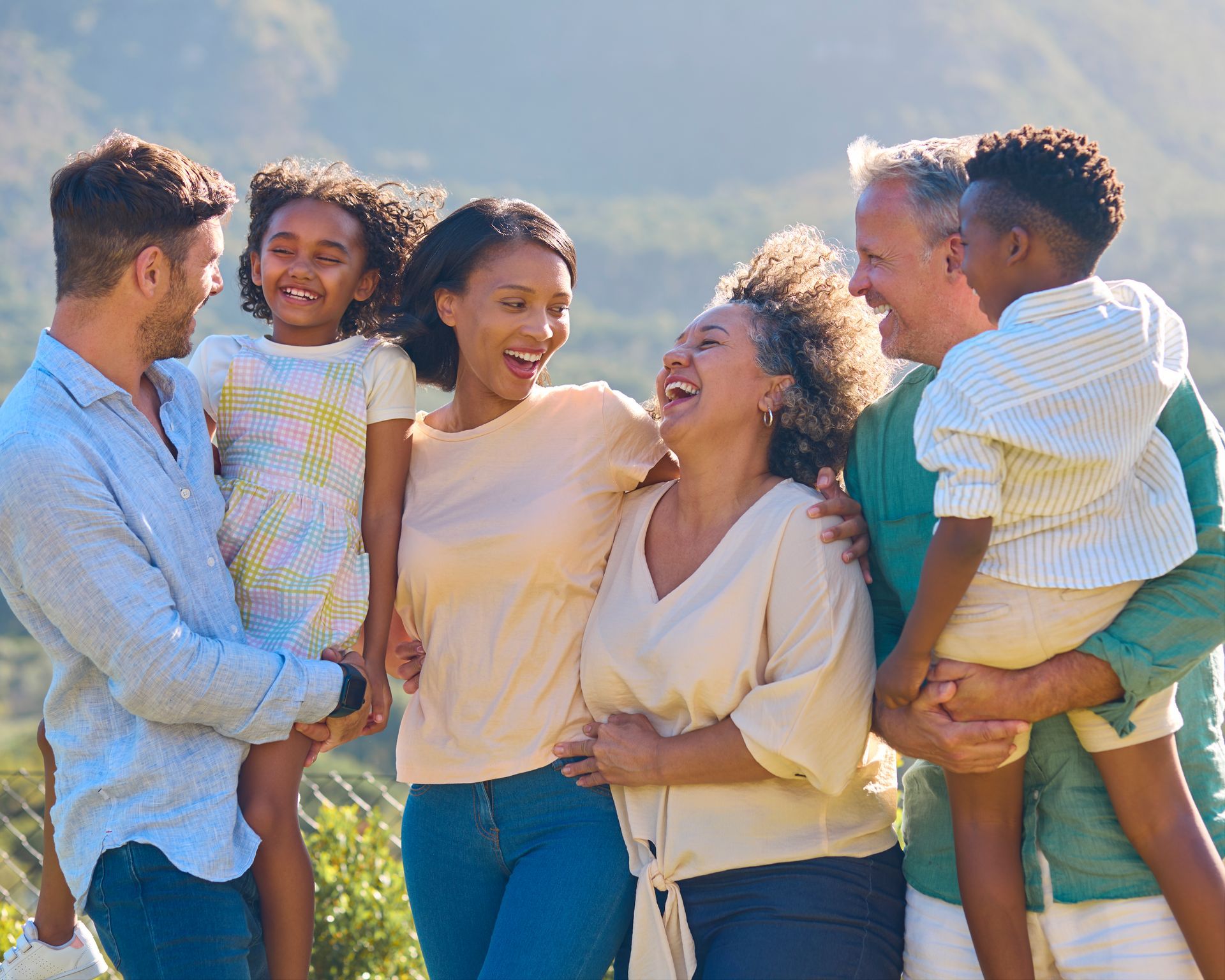 Group of six people laughing and hugging outdoors in bright sunlight