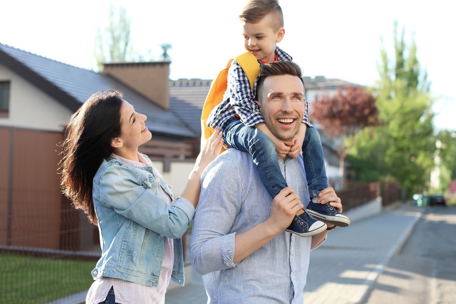 Two adults walking with a child on shoulders along a sunny suburban street